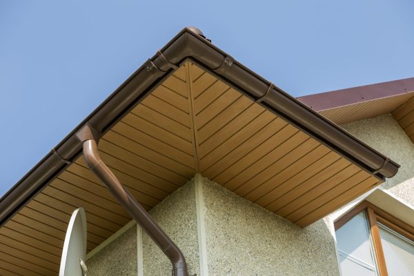 Bottom view detail of new modern house top with decorative lamp and satellite dish on stucco walls, plastic attic window, gutter pipe system on blue sky copy space background. Real estate concept.